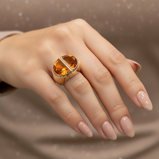 Hand wearing a gold ring with a large orange gemstone on a neutral background