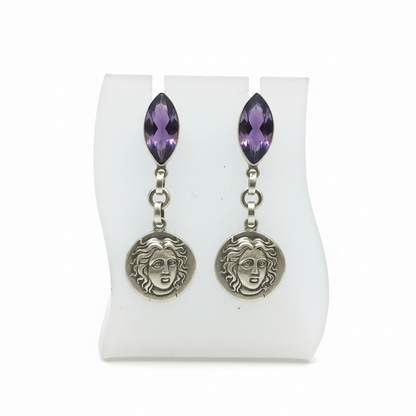 Pair of earrings with purple gemstones and face-like charms on a white display card.