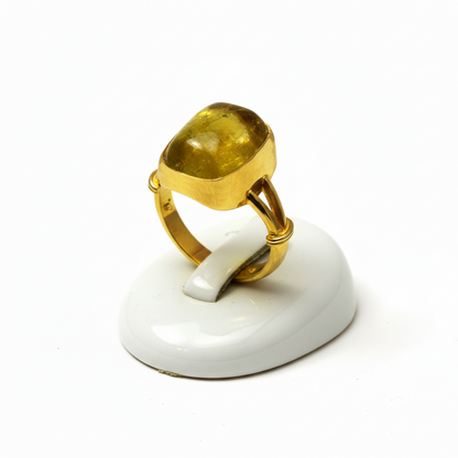 Gold ring with a green gemstone on a white stand against a white background