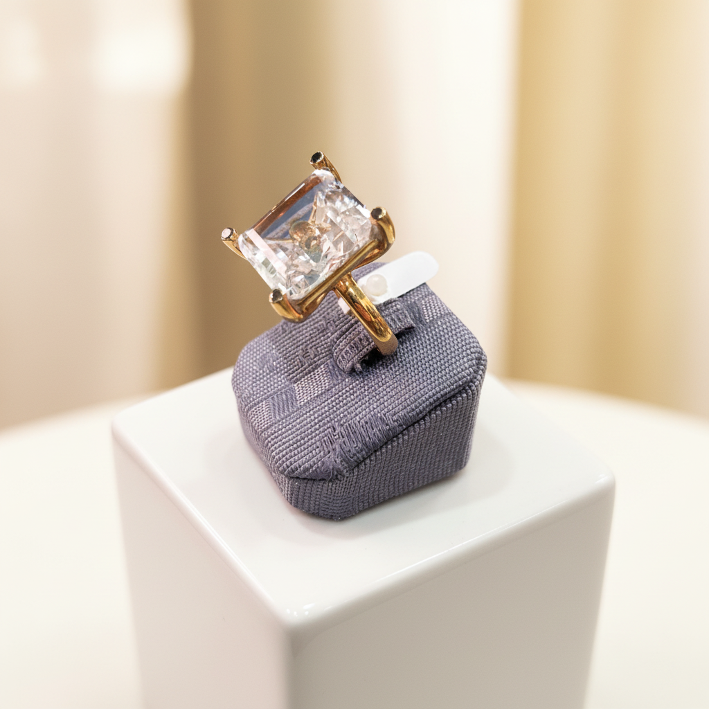 Gold ring with a large diamond on a textured gray stand against a neutral background