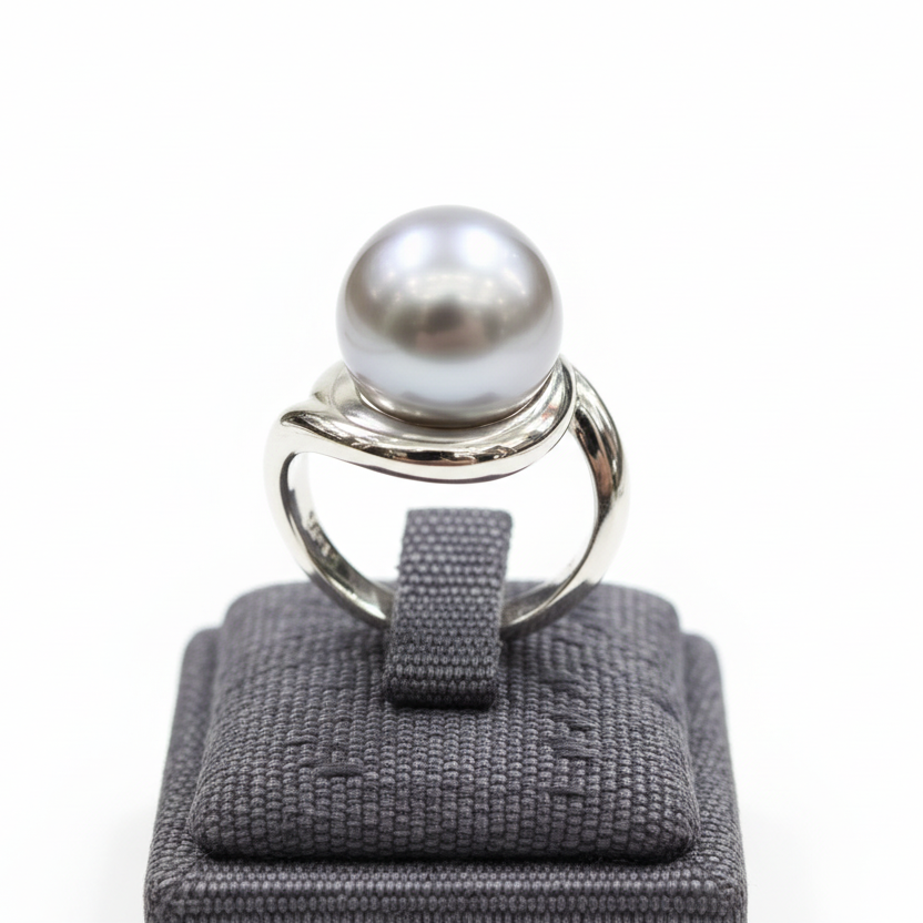 Silver ring with a large pearl on a gray ring cushion against a white background