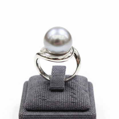 Silver ring with a large pearl on a gray ring cushion against a white background