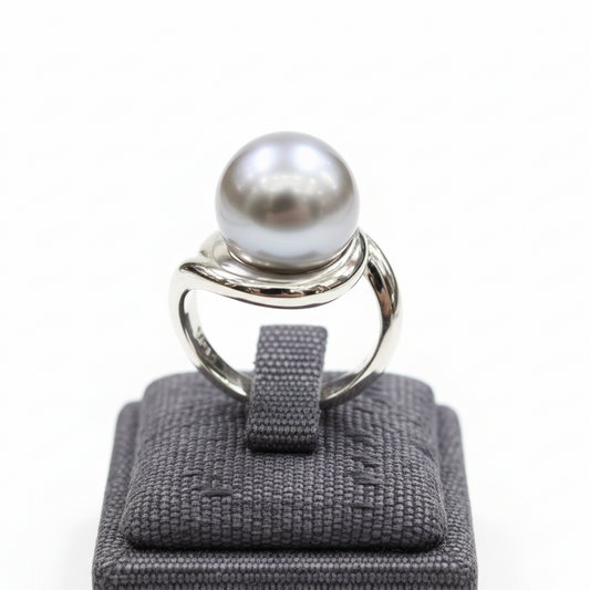 Silver ring with a large pearl on a gray ring cushion against a white background