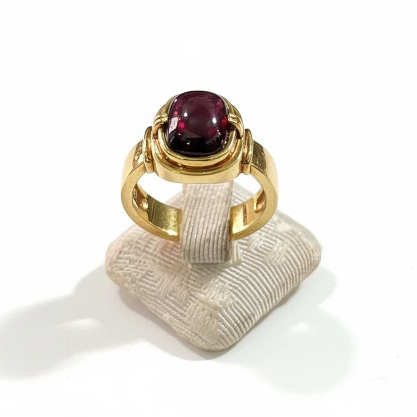 Gold ring with a red gemstone on a textured white stand