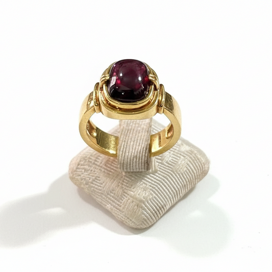 Gold ring with a red gemstone on a textured white stand