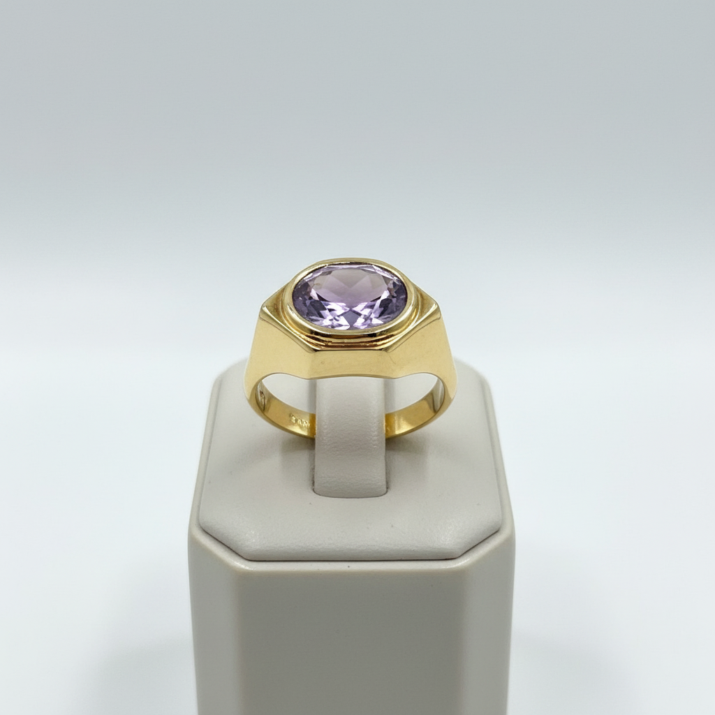 Gold ring with a purple gemstone on a white stand against a light gray background