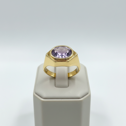 Gold ring with a purple gemstone on a white stand against a light gray background