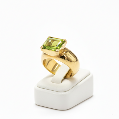 Gold ring with a green gemstone on a white stand against a white background