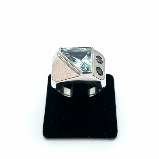 Silver ring with a large green gemstone on a black stand against a white background