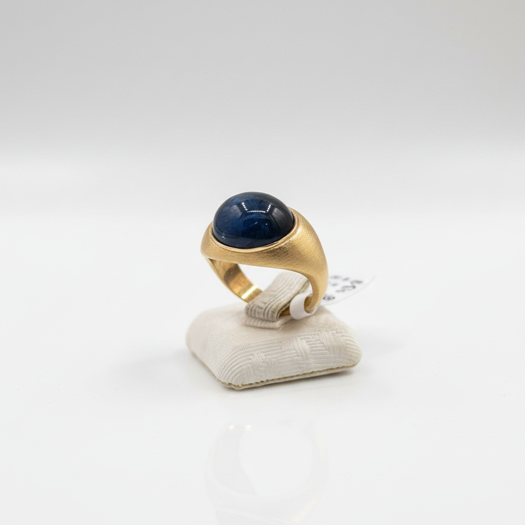 Gold ring with a blue gemstone on a white stand against a white background