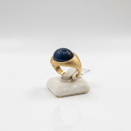 Gold ring with a blue gemstone on a white stand against a white background