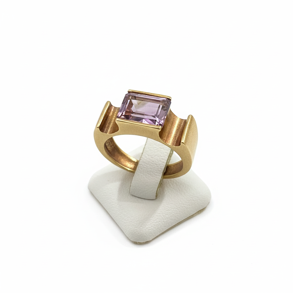 Gold ring with a purple gemstone on a white stand against a white background