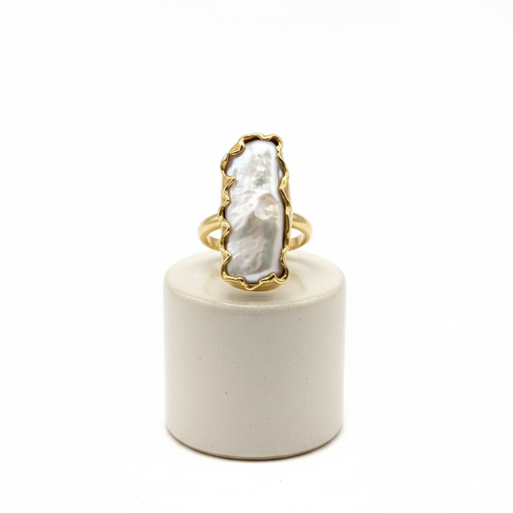 Gold ring with a large white stone on a white cylindrical stand against a white background