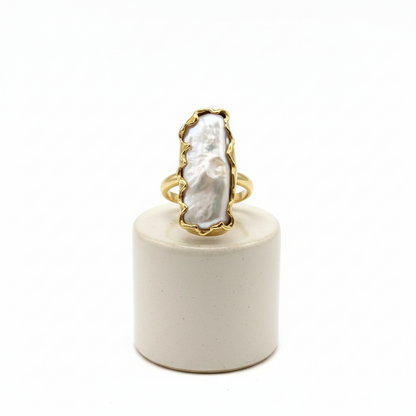 Gold ring with a large white stone on a white cylindrical stand against a white background
