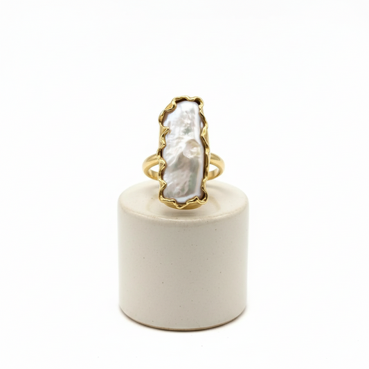 Gold ring with a large white stone on a white cylindrical stand against a white background