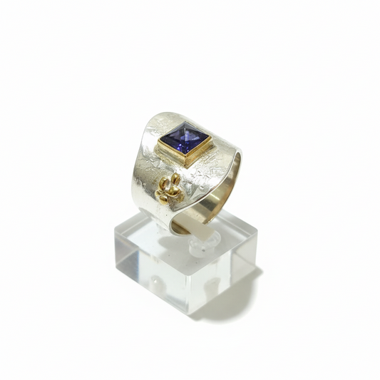 Gold ring with a purple gemstone on a clear stand against a white background
